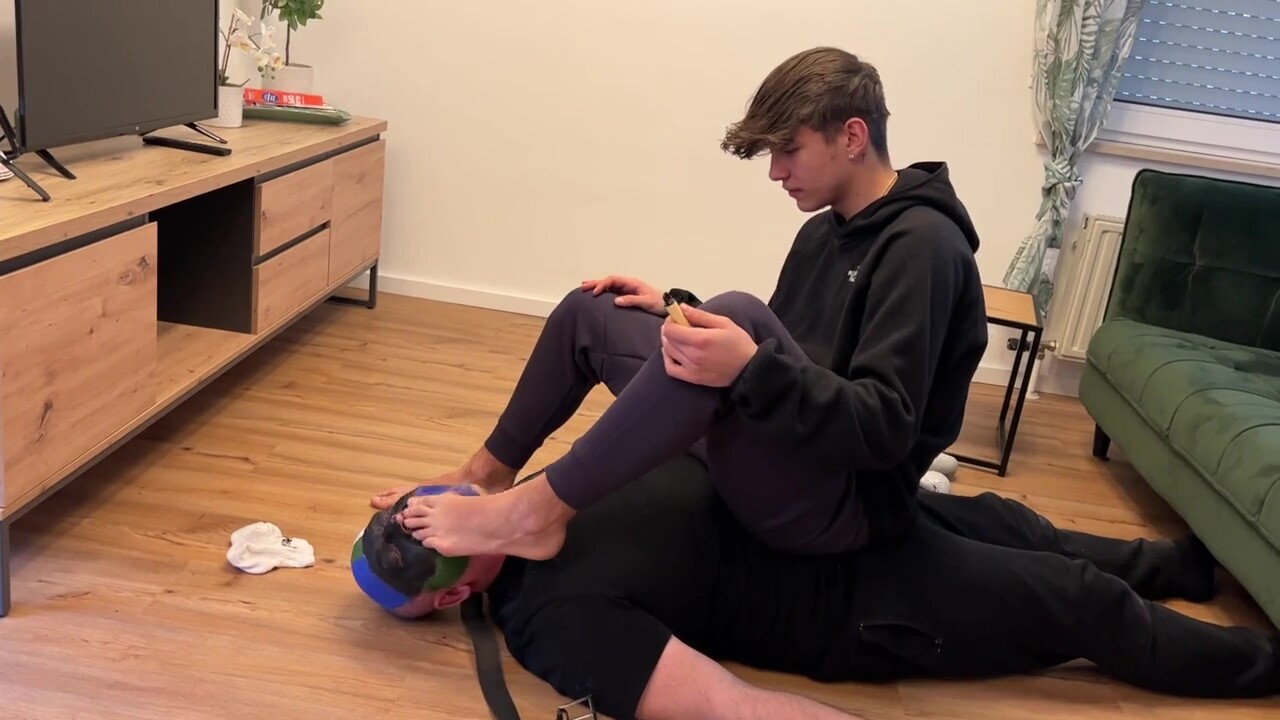 German master sitting on feet licking boy