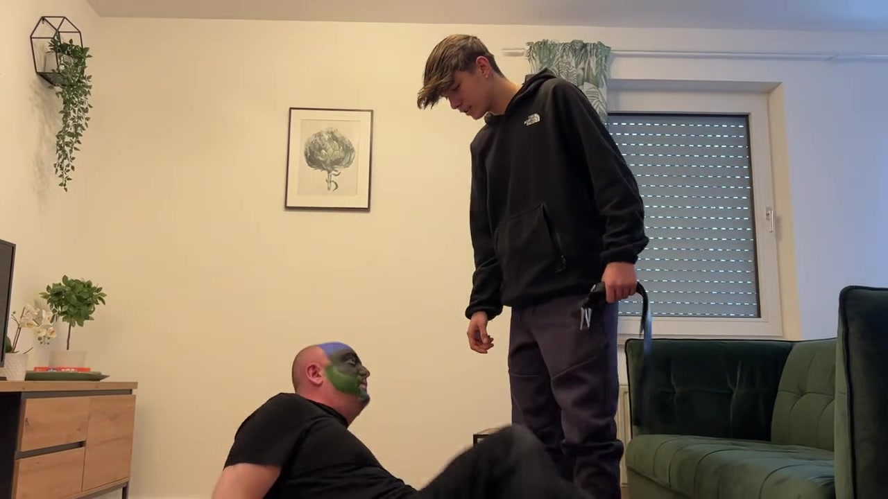 German master sitting on feet licking boy